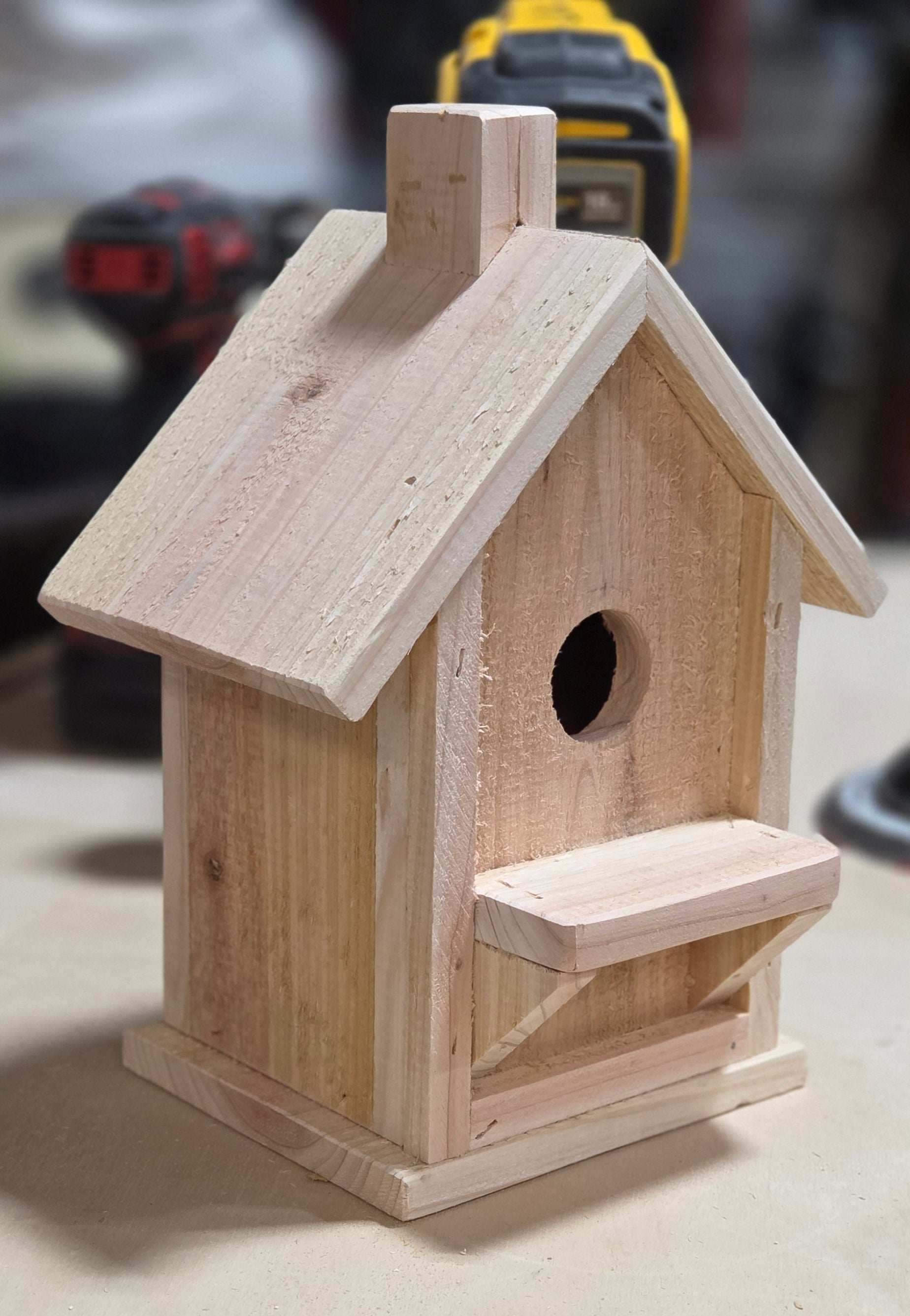 Wooden birdhouse attached to a wall with tools in the background